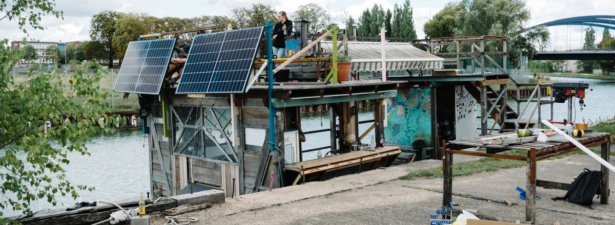 Kai am Kanal mit einem Floß, dass einige Holzaufbauten und PV Module trägt.